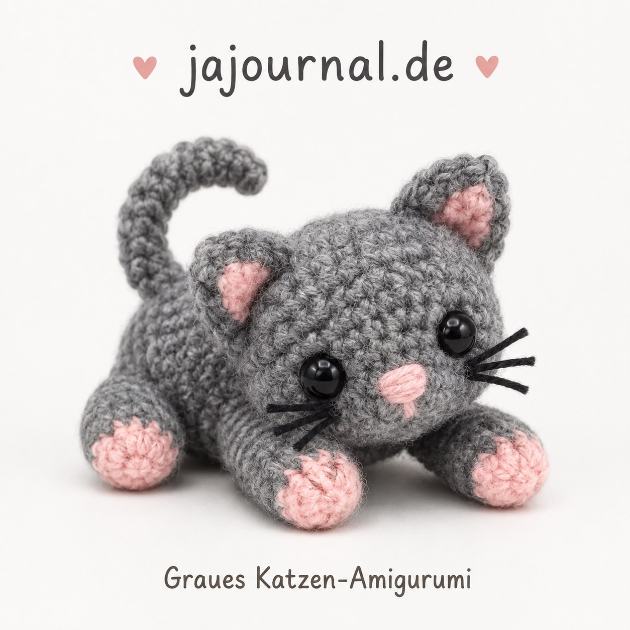 Graues Katzen-Amigurumi in geduckter Sprungpose mit rosa Pfoten und aufgestelltem Schwanz