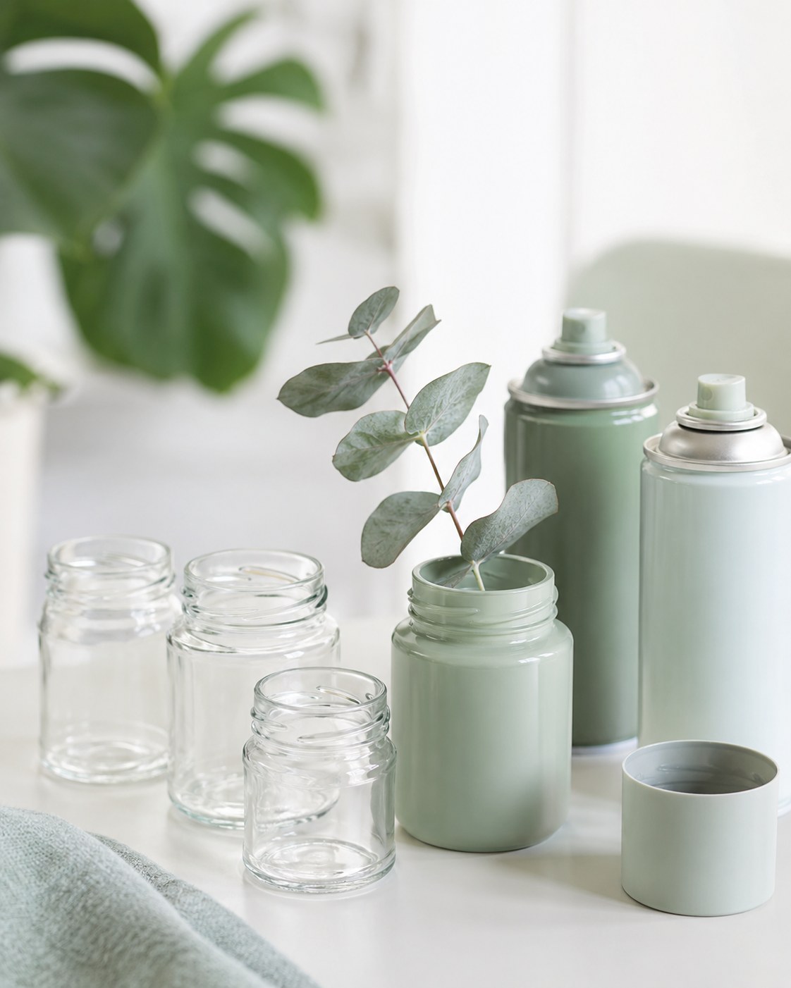 Salbeigrün besprühte Tablettenflaschen als Vasen neben Eukalyptuszweigen, ein Beispiel fürs Tablettenflaschen Upcycling